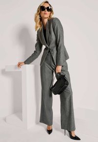 Grijs pinstripe pak met een getailleerde blazer en wijde broekspijpen. Zwarte patenten handtas en stilettohakken. Grote zwarte zonnebril.