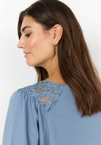 Blusa azul con detalles de encaje en los hombros. Confeccionada en una tela suave, tiene un corte holgado y mangas abullonadas.