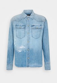 Jasnoniebieska koszula dżinsowa z guzikowym zapięciem z przodu, dwoma kieszeniami na piersi i wyraźnymi przetarciami na dolnej lewej stronie.