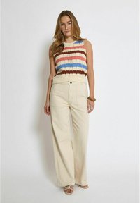 Top senza maniche lavorato a maglia con strisce rosse, blu, beige e marroni; pantaloni a vita alta, larghi e crema; abbinati a sandali con cinturini.