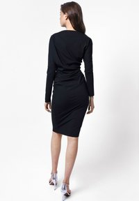 Czarna długa sukienka z długimi rękawami o dopasowanym fasonie, z marszczeniem z tyłu i długości do kolan. Połączona z srebrnymi butami na wysokim obcasie.