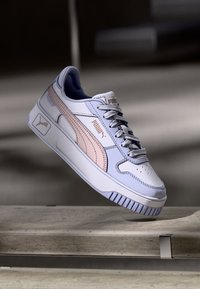 Valkoiset sneakersit, joissa on vaaleanlila ja vaaleanpunainen korostus, rei'itetty varvasosa, litteät nauhat ja paksu kumipohja, jossa on vaaleita uria.