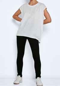 T-shirt bianco largo con scollatura rotonda e maniche corte, abbinato a leggings neri aderenti e scarpe da ginnastica bianche.