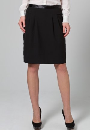 Zwarte knie-lange rok met plooien aan de voorkant, een gladde textuur en een contrasterende satijnen tailleband, gecombineerd met zwarte hoge hakken.