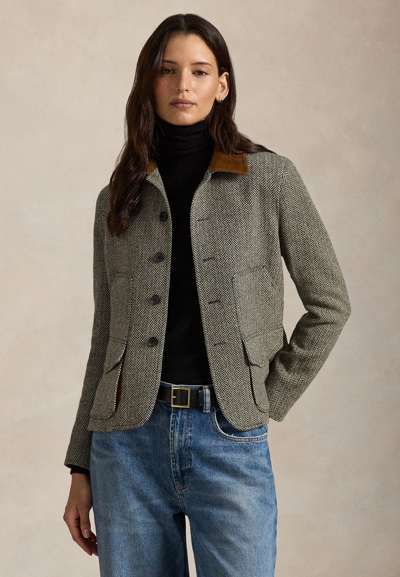 Kurtka w wzór pepitki w odcieniach szarości i czerni, z brązowym kołnierzem z zamszu, wyposażona w przednie kieszenie i dopasowany krój. W zestawie z czarnym golfem.