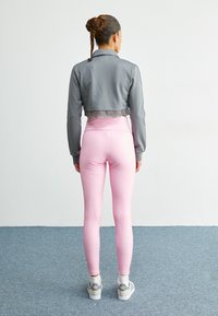 Kuttet grå jakke med blonderkant, kombinert med tettsittende rosa leggins og grå joggesko. Glatte teksturer og minimalistisk design.