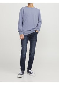 Sudadera azul claro de cuello redondo con puños acanalados, combinada con unos pantalones vaqueros skinny azul oscuro. Zapatillas blancas con detalles en azul marino completan el atuendo.