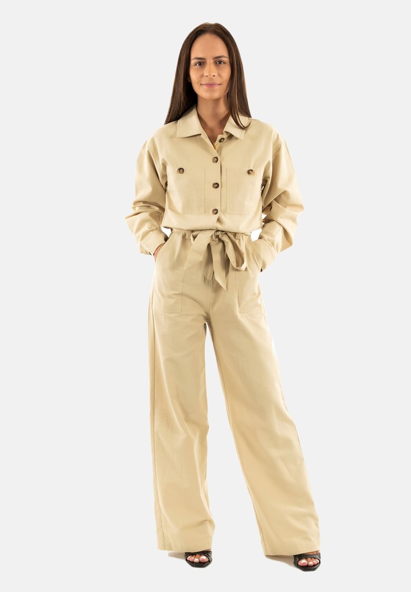 Conjunto de dos piezas beige que incluye una camisa de botones con cuello y bolsillos en el pecho, y pantalones de pierna ancha atados a la cintura con un cinturón a juego.