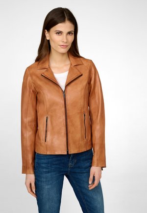 Veste en cuir marron avec un design ajusté, col cranté, fermeture éclair à l'avant et deux poches latérales zippées. Associée à un jean bleu.