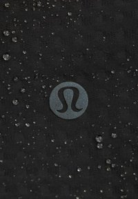 Sort struktureret stof med vanddråber; har et cirkulært logo i mørkegrå i midten. Materialet udviser en subtil glans.
