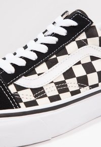 Sort-hvid ternet lærreds sneakers med hvide snørebånd og et hvidt side-logo. Har en tekstureret ydersål og syningsdetaljer.