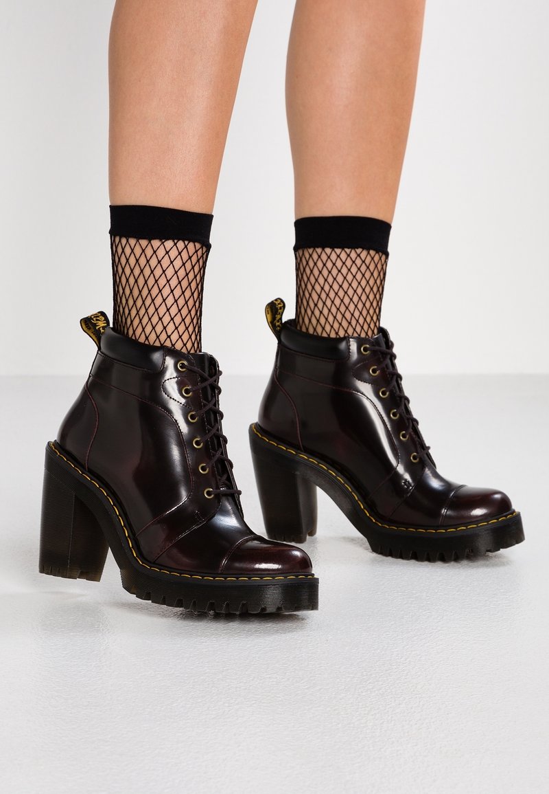 Bottes montantes bordeaux foncé à lacets avec une finition brillante, talon carré noir, semelle texturée, coutures jaunes et chaussettes en mesh noir.