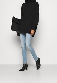 Sudadera negra de gran tamaño con mangas largas, combinada con jeans ajustados de color azul claro y botas de tobillo negras y puntiagudas. Accesorio: bolso negro acolchado.