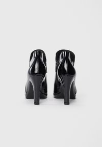 Chaussures à talons aiguilles en cuir verni noir avec une fermeture éclair à l'arrière, présentant une finition lisse et brillante ainsi qu'une forme de talon effilée.