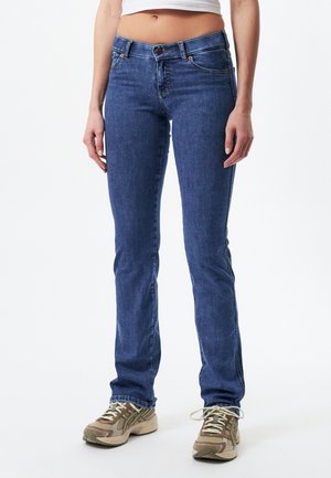Blue denim jeans with a straight leg design, five pockets, a button closure, and a subtle textured finish. Paired with beige athletic shoes.