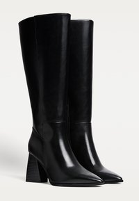 Bottes noires montantes en cuir lisse, avec des bouts pointus et un talon bloc au design à rainures verticales. Fermeture éclair sur le côté.