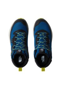 Plave sportske cipele s mrežastim gornjim dijelom, crnim detaljima, žutim vezicama i teksturiranim potplatom. Imaju petlju za povlačenje na stražnjoj strani. Model: The North Face.