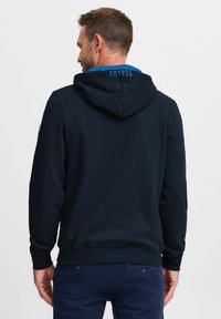 Felpa blu navy con tessuto liscio, cordino regolabile, dettaglio blu nel colletto e un piccolo logo sulla manica.
