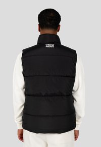 Gilet imbottito nero con colletto alto, caratterizzato da pannelli cuciti e un logo bianco sul retro. Texture liscia, design leggero.