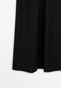 Svart knälång kjol gjord av ett slätt tyg. Har en enkel design med rakt fåll och inga synliga mönster eller detaljer.