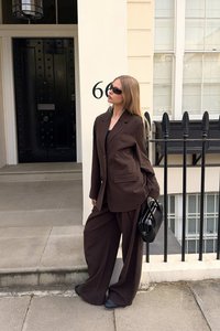 Blazer marrón de gran tamaño y pantalones de pierna ancha a juego. Los accesorios incluyen un bolso negro y gafas de sol. Tejido suave, diseño a medida.