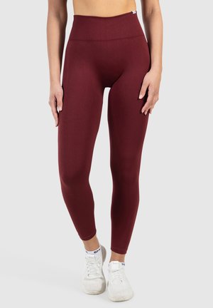 Hooggesneden kastanjebruine legging gemaakt van rekbaar materiaal, met een gladde textuur en een nauwsluitend ontwerp, gecombineerd met witte sportschoenen.