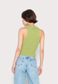 Top sem mangas de malha canelada em verde claro com gola alta, combinado com jeans de denim azul claro com bolsos traseiros.
