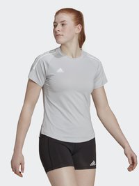 Camiseta atlética gris de manga corta, con logotipos de Adidas blancos y acentos de rayas. Combinada con pantalones cortos atléticos negros.