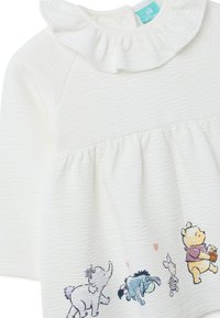 Weißes Baby-Kleid mit langen Ärmeln und rüschigem Kragen, das bunte Illustrationen von Winnie Puuh, Ferkel, Tigger und einem Elefanten auf dem Rock zeigt.