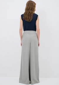 Grijze wijde broek van soepel materiaal, met een hoge tailleband en subtiele achterzakdetails, gecombineerd met een marineblauw mouwloos topje.