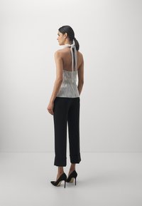 Srebrna naborana halter vrhnja, otvorenog leđa, u paru s crnim skraćenim hlačama i crnim štiklama. Glatka tekstura s elegantnim dizajnom.