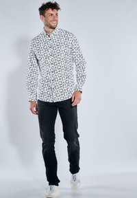 Weißes Hemd mit Knopfverschluss und schwarzem Blattmuster, kombiniert mit schwarzen Hosen und weißen Sneakern. Glatte Stoffqualität mit klassischem Kragendesign.