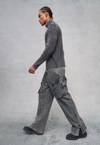 Suéter gris de cuello alto acanalado con mangas ajustadas, combinado con pantalones cargo grises sueltos que cuentan con bolsillos y un dobladillo deshilachado, llevados con botas negras.