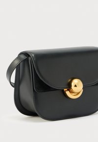 Schwarze Lederhandtasche mit geschwungener Klappe und glänzendem, rundem Goldverschluss, ausgestattet mit kurzem Riemen zum Tragen in der Hand oder über der Schulter.