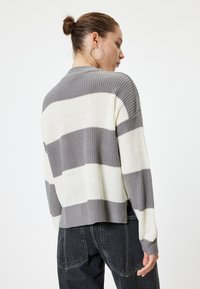 Gestreepte gebreide trui in grijs en crème met een geribbelde textuur. Beschikt over een licht cropped snit en lange mouwen, gestyled met donkere spijkerbroek.