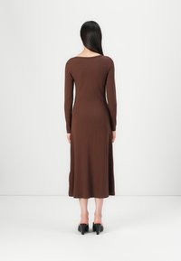 Brun ribbet langermet kjole med rund hals, tettsittende bodice og flagrende hem, kombinert med svarte blokkhelte sko.