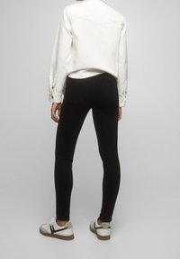 Svarta skinny jeans med en slät yta, åtsittande design och bakfickor, bärs med en vit långärmad skjorta och avslappnade sneakers.