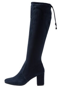 Knähöga marinblå stövlar gjorda av mjuk mocka, med fyrkantig tå och tjock klack. Har en dragflik och justerbar dragsko vid toppen.