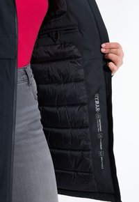 Černá nepromokavá bunda s prošívanou černou podšívkou, obsahující boční kapsu a štítky označující nepromokavost, větruodolnost a prodyšnost.