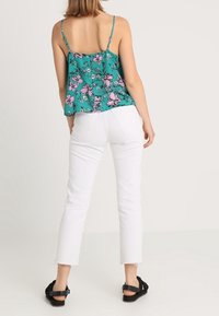 Miętowa bluzka na ramiączkach w kwiaty z różowymi motywami, połączona z białymi ściętymi dżinsami. Stylizacja charakteryzuje się cienkimi ramiączkami i postrzępionymi detalami na dole. Czarne sandały.