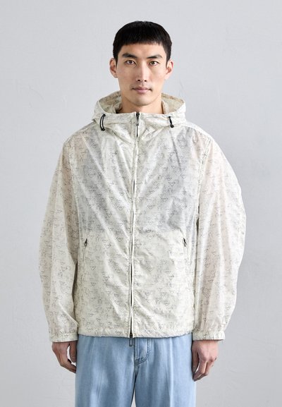 Chaqueta ligera y con estampado en beige translúcido con gráficos negros, que cuenta con capucha, puños elásticos y bolsillos con cremallera.