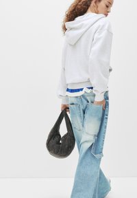 Grå hættebluse med ribbet kanten, lagdelt over en blå top med hvid flæse. Lyseblå oversized jeans med en taske i mørk denim.
