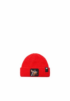 Bonnet rouge en tricot avec un revers, un écusson représentant un chien et portant l’inscription « Beware », et une petite étiquette noire.