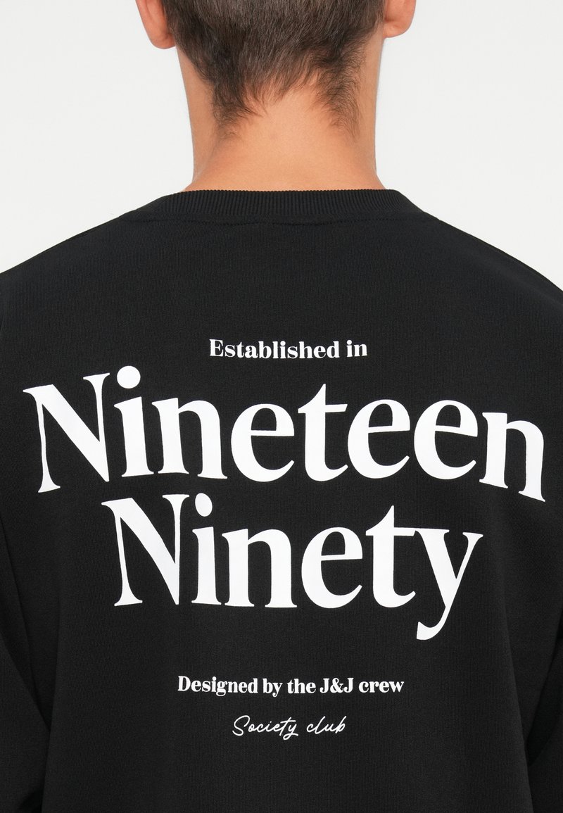 Sweatshirt noir avec un grand texte blanc au dos : "Établi en mille neuf cent quatre-vingt" et "Conçu par le club de la société J&J crew."