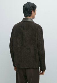 Giacca in suede marrone con colletto in pelle liscia. La schiena presenta un design semplice e un taglio dritto. Superficie testurizzata con dettagli minimi.