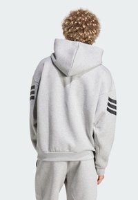 Sweat à capuche gris en tissu doux, avec une coupe ample, un ourlet côtelé et des accents noirs à trois bandes sur les deux manches.