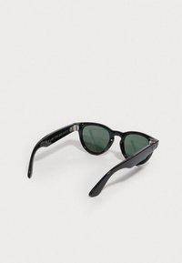 Occhiali da sole cat-eye neri con lenti verdi. Presentano una montatura in plastica elegante e bracci robusti. Marchio ben visibile sul lato.