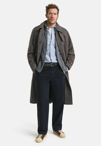 Brauner karierten Mantel, graue Innenjacke, hellblaue Hemd, dunkle Hose und zweifarbige Schuhe. Verfügt über Knopfverschlüsse und Taschen.