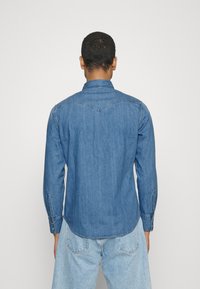 Blå denimskjorta med lång ärm, spetsig krage och knäppte ärmslut. Har en ok-design och en slät, texturerad och mjuk kvalitet.