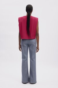 Haut sans manches rouge avec des plis verticaux, associé à un jean évasé bleu clair avec des coutures contrastées. Tissu lisse et coupe ajustée.
